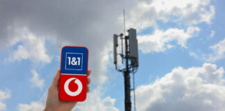 Smartphone mit Logos von Vodafone und 1&1 vor einem Funkmast