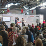 Ein Stand des Deutschlandradios auf der Frankfurter Buchmesse, Publikum hört einem stehenden Redner zu