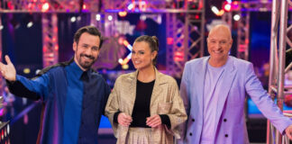 Jan Köppen, Laura Wontorra und Frank (Buschi) Buschmann stehen nebeneinander im Ninja-Warrior-Studio und lachen in die Kamera