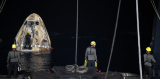 Drei Arbeitende bereiten den Abtransport des schwimmenden "Crew Drageon Endeavour" vor, das im Hintergrund im Meer schwimmt.