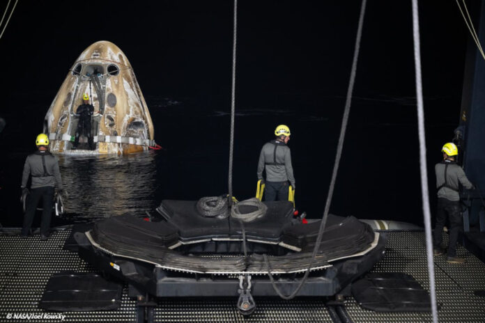 Drei Arbeitende bereiten den Abtransport des schwimmenden "Crew Drageon Endeavour" vor, das im Hintergrund im Meer schwimmt.