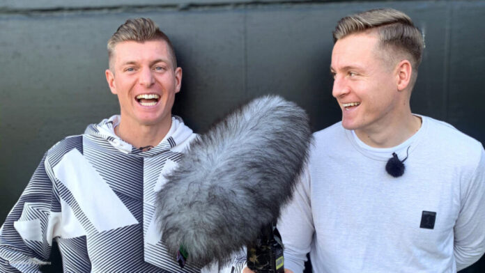 Toni Kroos und Felix Kroos lachen in die Kamera und halten ein Mikrofon.