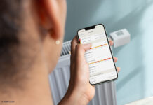 Jemand hält sein Smartphone, auf dem die Fritz!App gerade geöffnet ist, vor einen Heizkörper