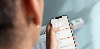Jemand hält sein Smartphone, auf dem die Fritz!App gerade geöffnet ist, vor einen Heizkörper