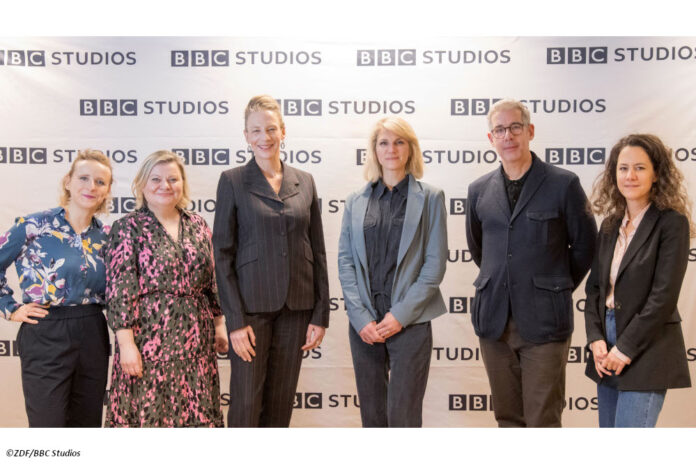 Eine Gruppe von Menschen steht vor einer Werbewand, auf der "BBC Studios" steht