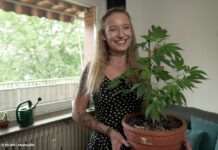 Eine Frau präsentiert eine Cannabis-Pflanze im Topf.